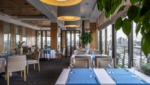 Restaurante com mesas preparadas para refeições, grandes janelas com vista para a cidade e design de interiores moderno.