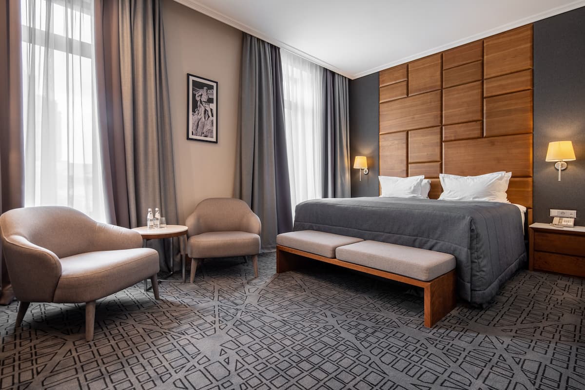 A hotel room with a bed, two armchairs, a small table, and a bench.