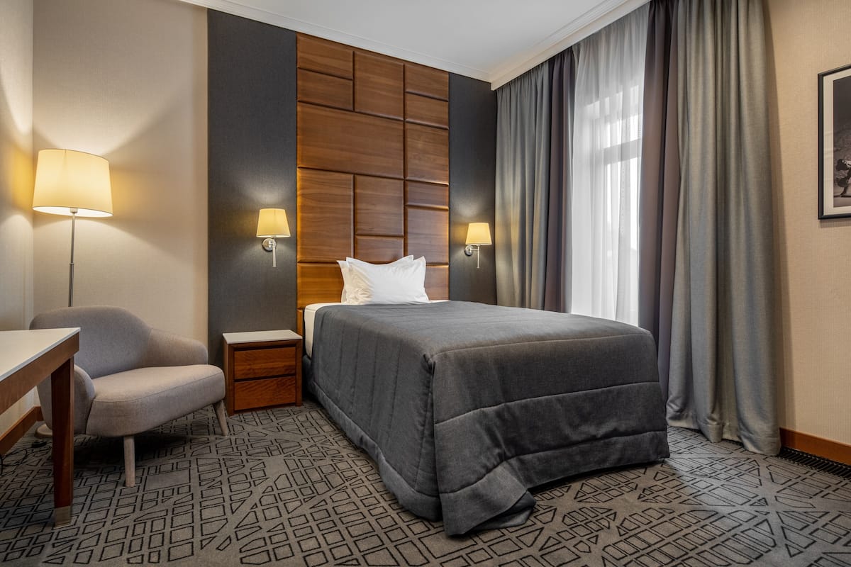 A hotel room with a bed, a desk, a chair, two bedside tables, and a wall panel.