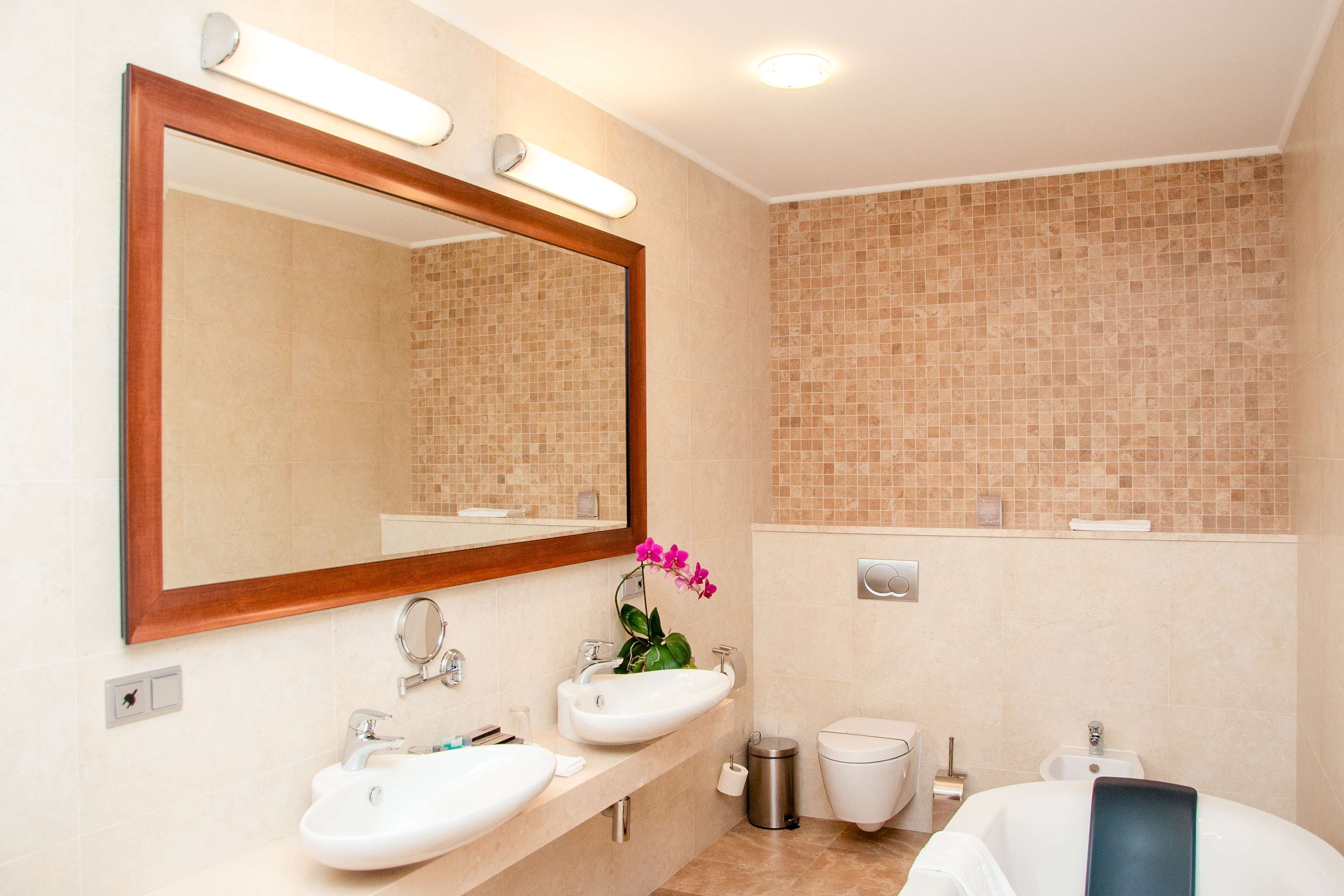 Un baño moderno con un espejo grande, dos lavamanos, un inodoro y una bañera.
