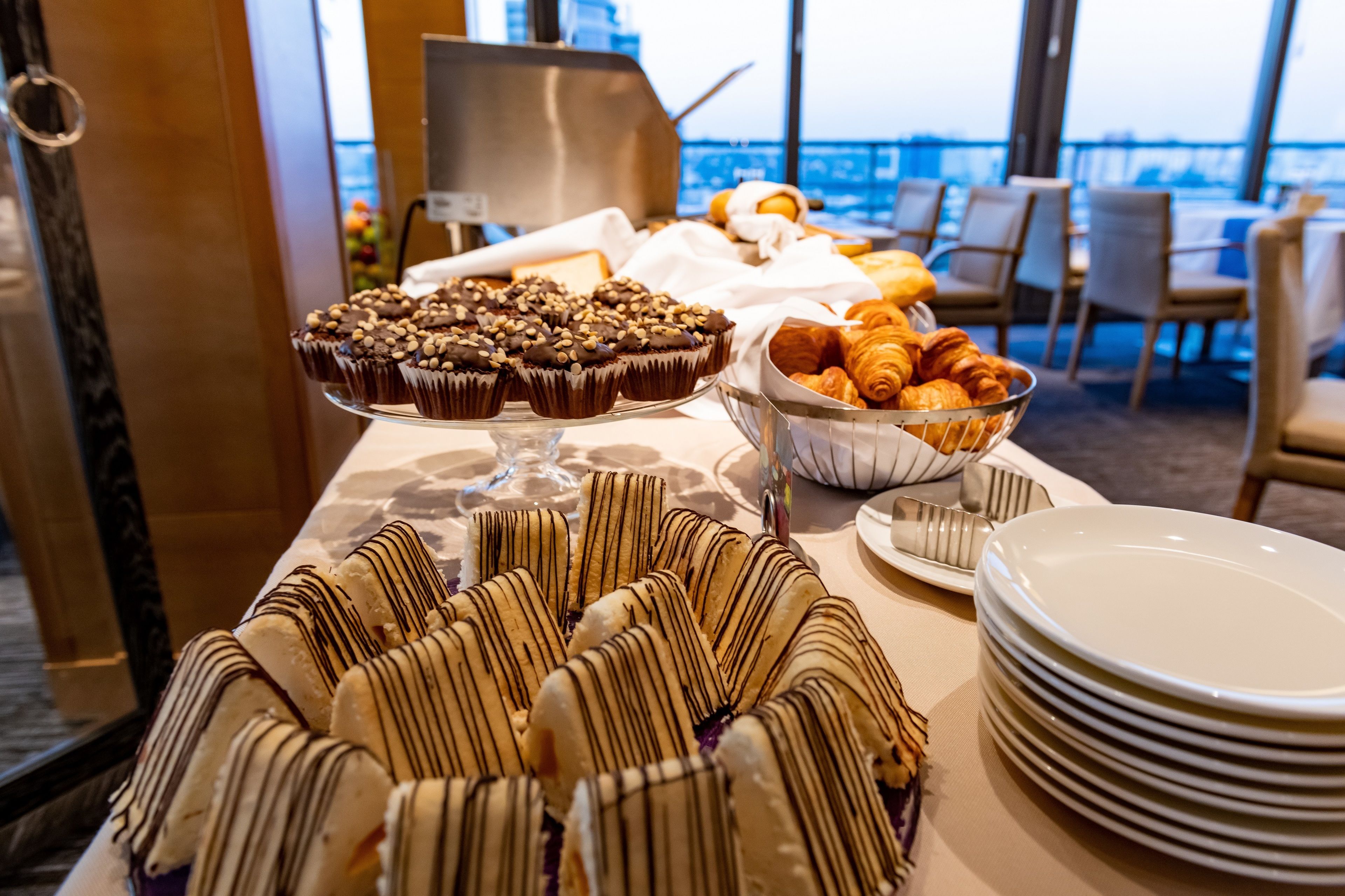 Ein reichhaltiges Buffet mit verschiedenen Backwaren und Desserts, darunter Schokoladen-Cupcakes, Croissants und in weißer Schokolade getunkte Gebäcke.