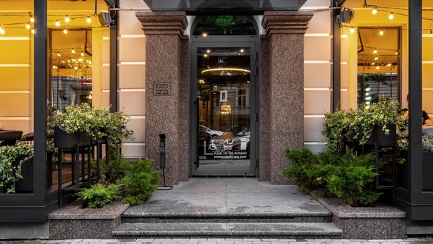 Entrada de um hotel urbano com fachada clássica, acesso coberto e um letreiro sobre as portas.