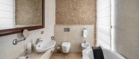 A modern bathroom with two sinks, a toilet, a bidet, and a bathtub.