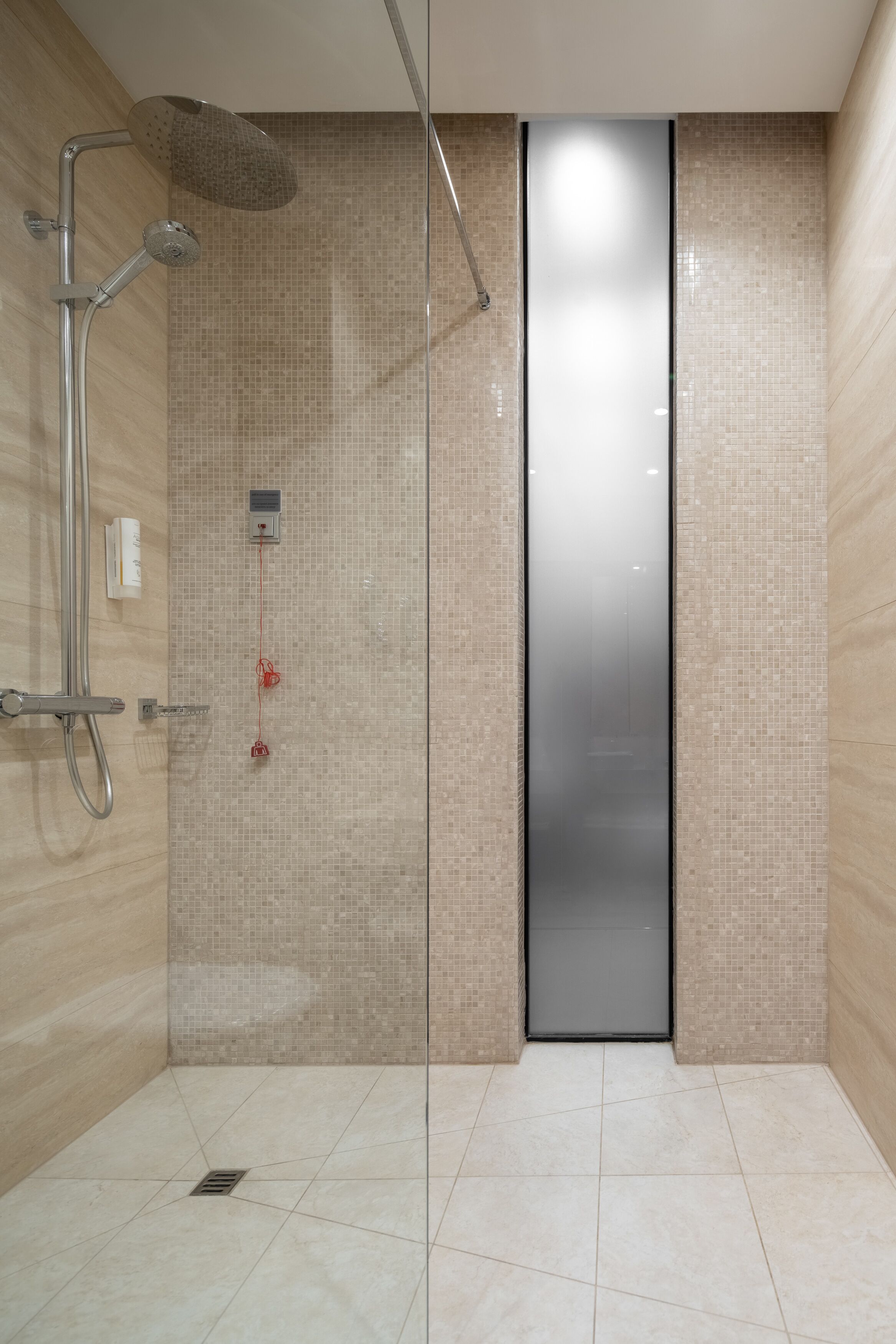 Une salle de bain moderne dotée d’une douche à parois de verre, de murs carrelés et d’un panneau de commande visible.