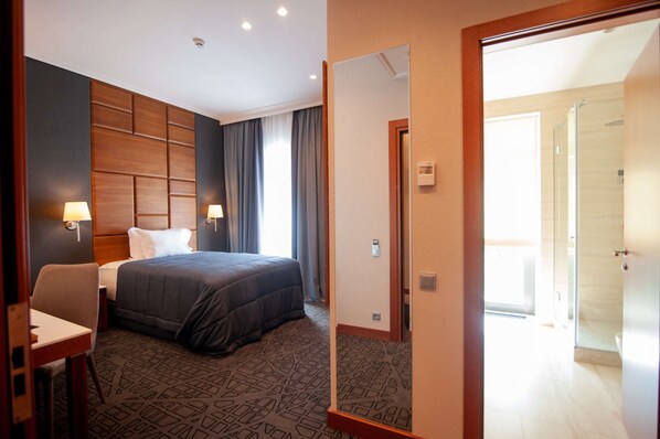 A hotel room with a bed, bedside lamps, a desk, and a bathroom visible through an open door.