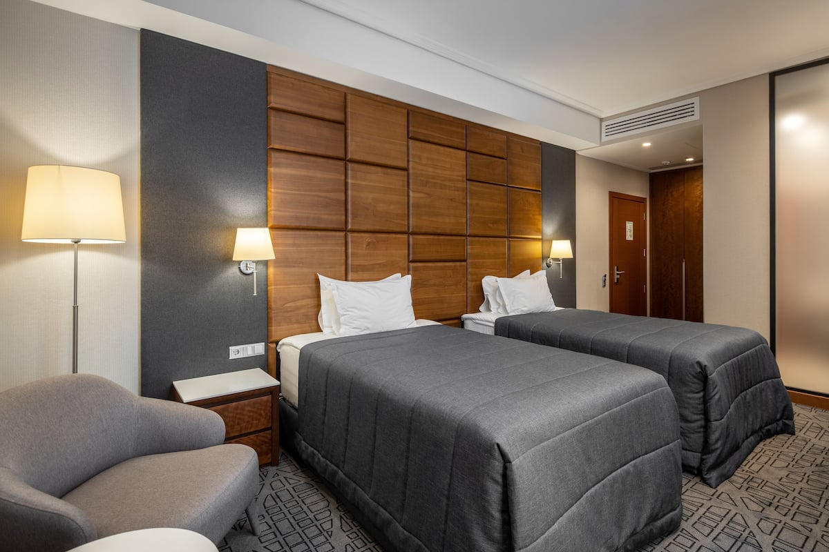 A hotel room with two beds, a chair, a nightstand, and a lamp.