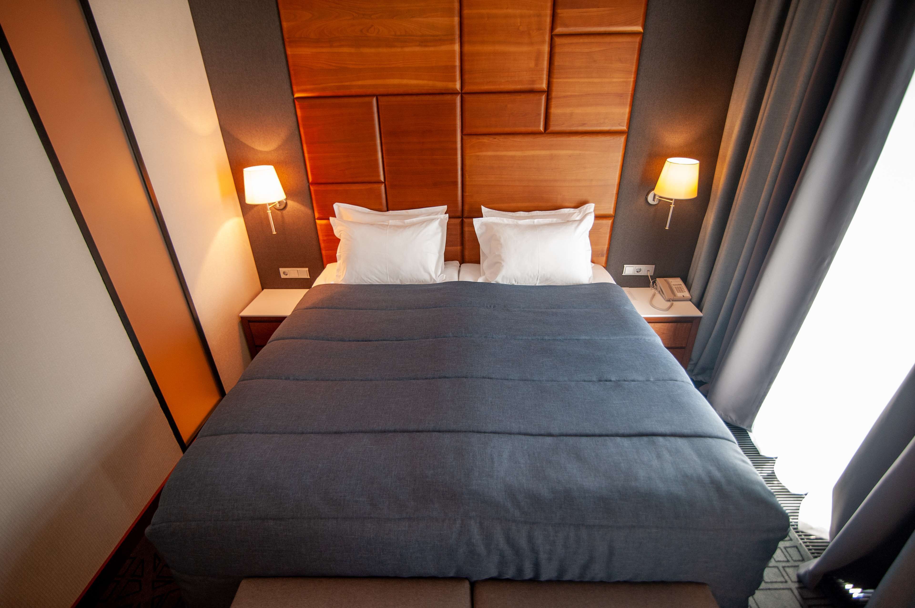 A hotel room with a large bed, two bedside lamps, and a wooden headboard.