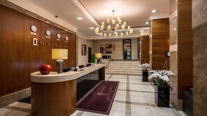 Uma área de recepção de hotel com um balcão de madeira, um candelabro e piso de mármore.