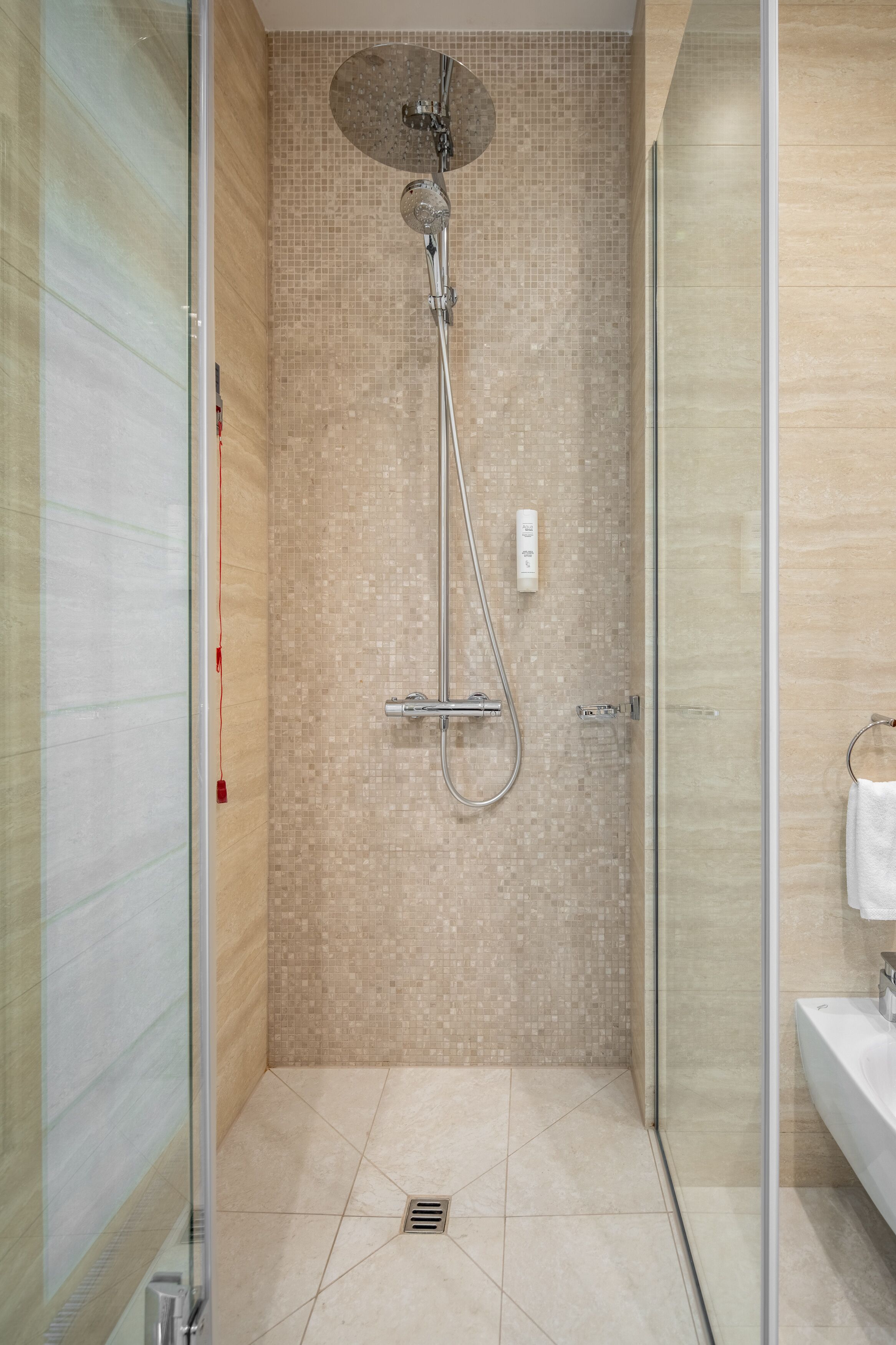 Un baño moderno con cabina de ducha de vidrio, paredes con azulejos y zona de lavamanos.