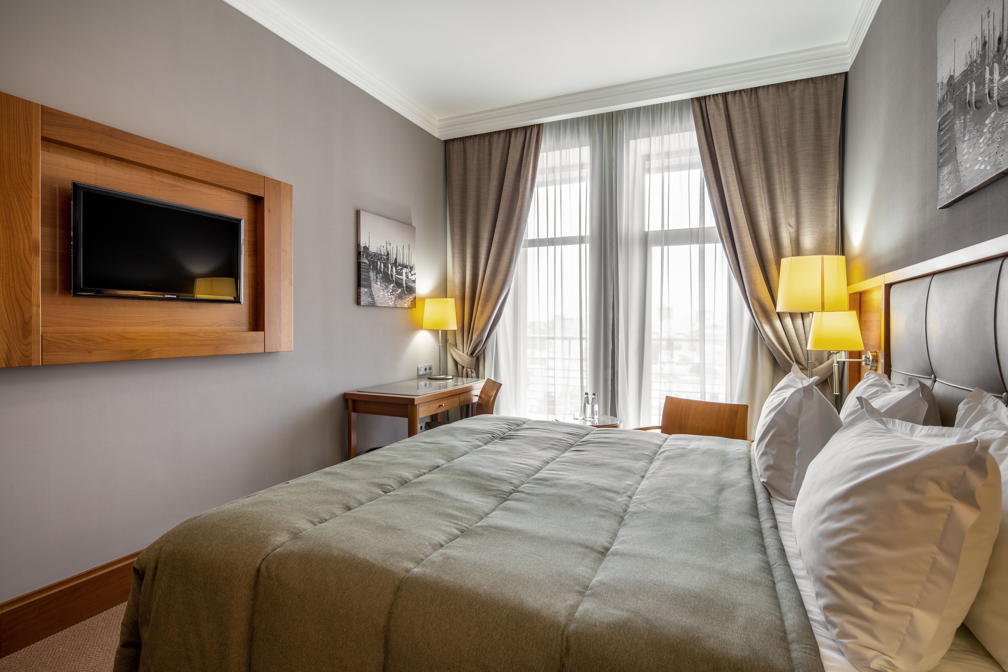 Een hotelkamer met een groot bed, een flatscreen televisie aan de muur, een bureau met een stoel, en twee lampen.