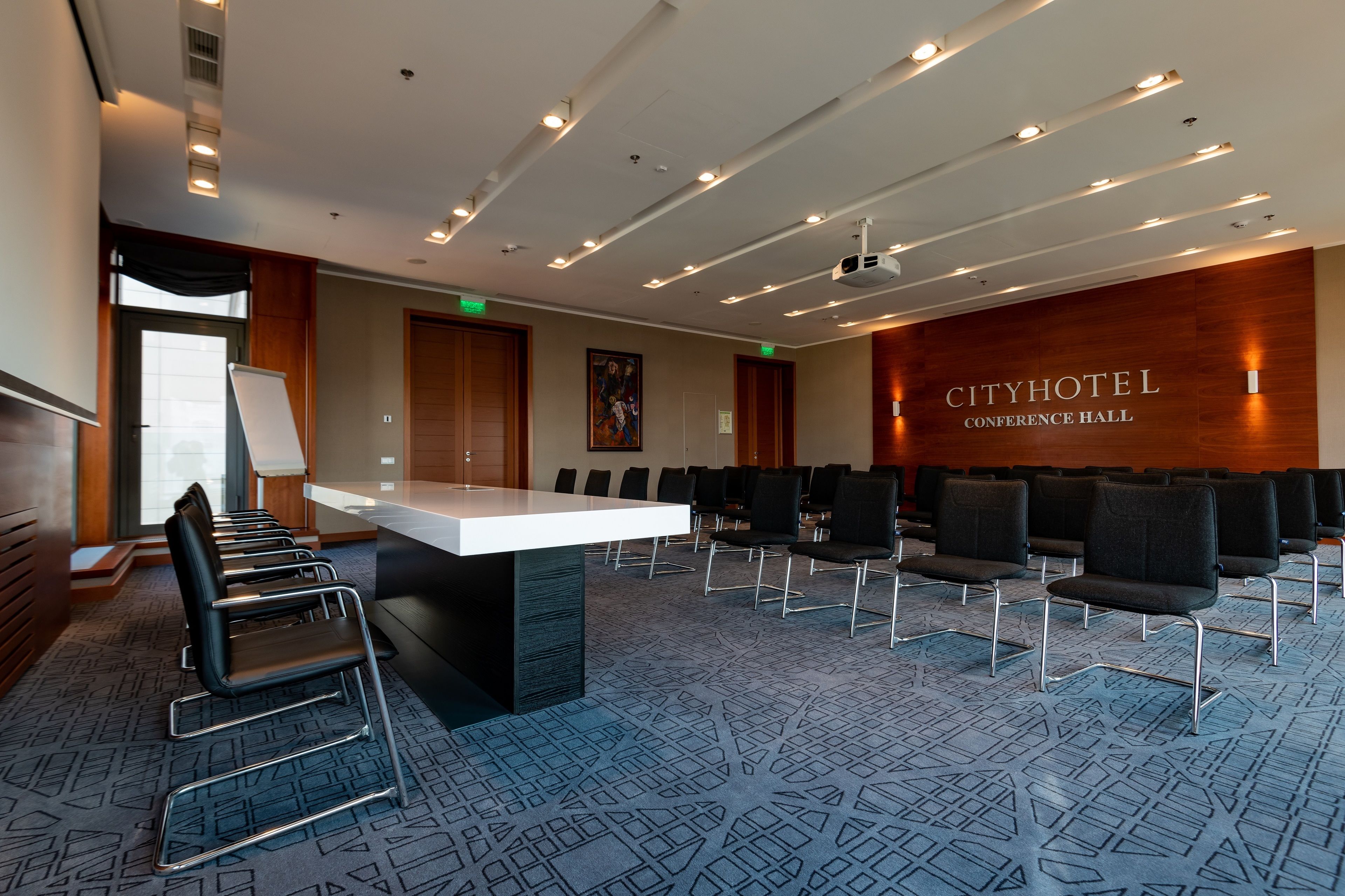 A conference room with a long table, rows of chairs, and a carpeted floor.