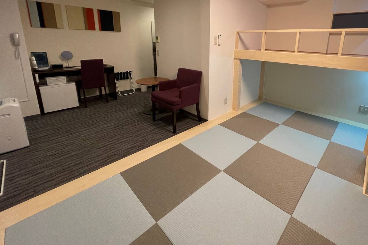 A room with a bunk bed, a desk, a chair, and a small table.