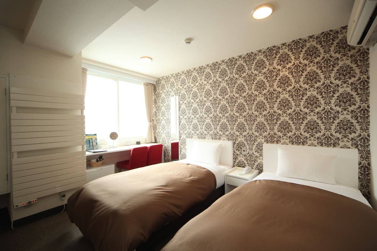 A hotel room with two beds, a desk, and a window.