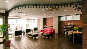 A spacious lobby with a red sofa, black chairs, and a wooden floor. There is a brick wall and a large window in the background.