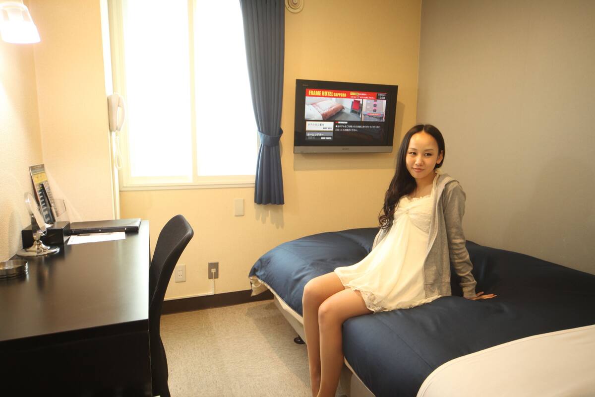 A hotel room with a bed, a desk with a phone, and a TV on the wall.