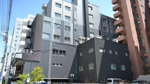 A multi-story building with balconies, a visible entrance, and a parking area with vehicles.