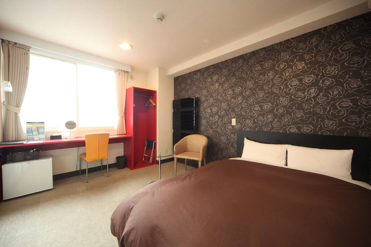 A hotel room with a bed, a desk, a chair, a television, and a window with curtains.
