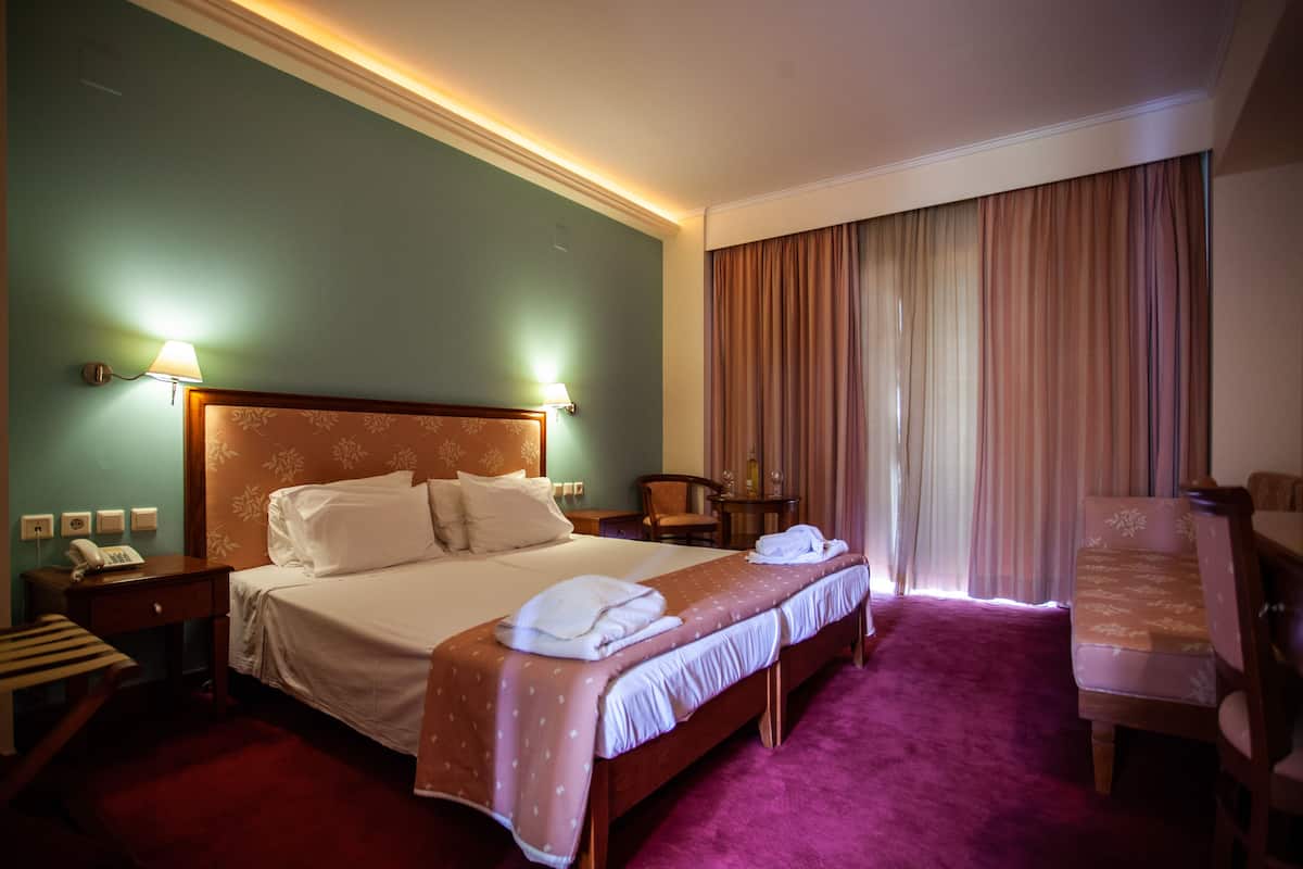 Una habitación de hotel con una cama grande, un escritorio con lámpara, una silla y una ventana con cortinas.