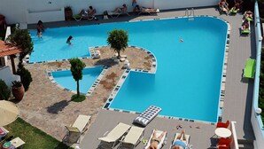 Área de piscina com espreguiçadeiras e uma pequena árvore.