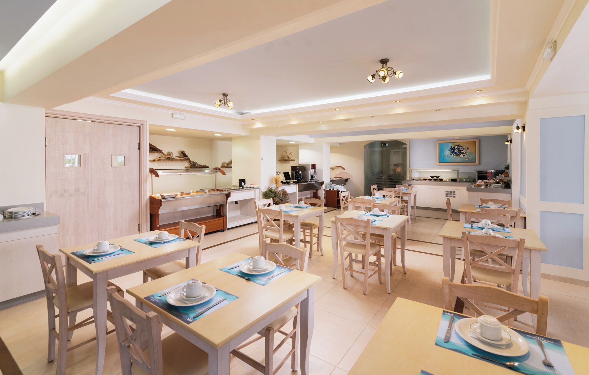 A spacious dining area with multiple tables and chairs, a kitchen in the background, and a modern ceiling design.