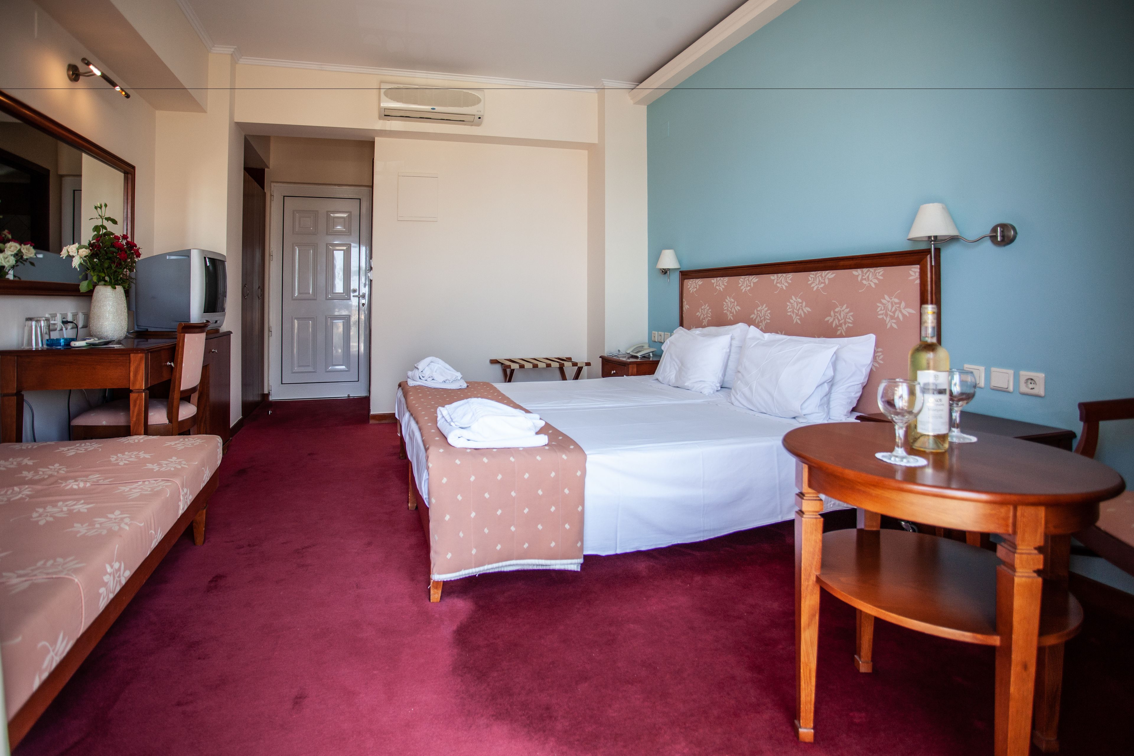 Quarto de hotel com duas camas, uma mesa, uma cadeira, uma televisão e uma mesa com copos.