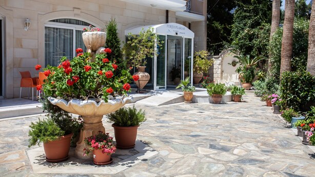 Entrada de hotel com um pátio de pedra, plantas em vasos e um grande vaso decorativo.
