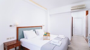 Quarto de hotel com uma cama, mesas de cabeceira, um criado-mudo, um tabuleiro com itens de café da manhã e uma porta que dá para outro cômodo.