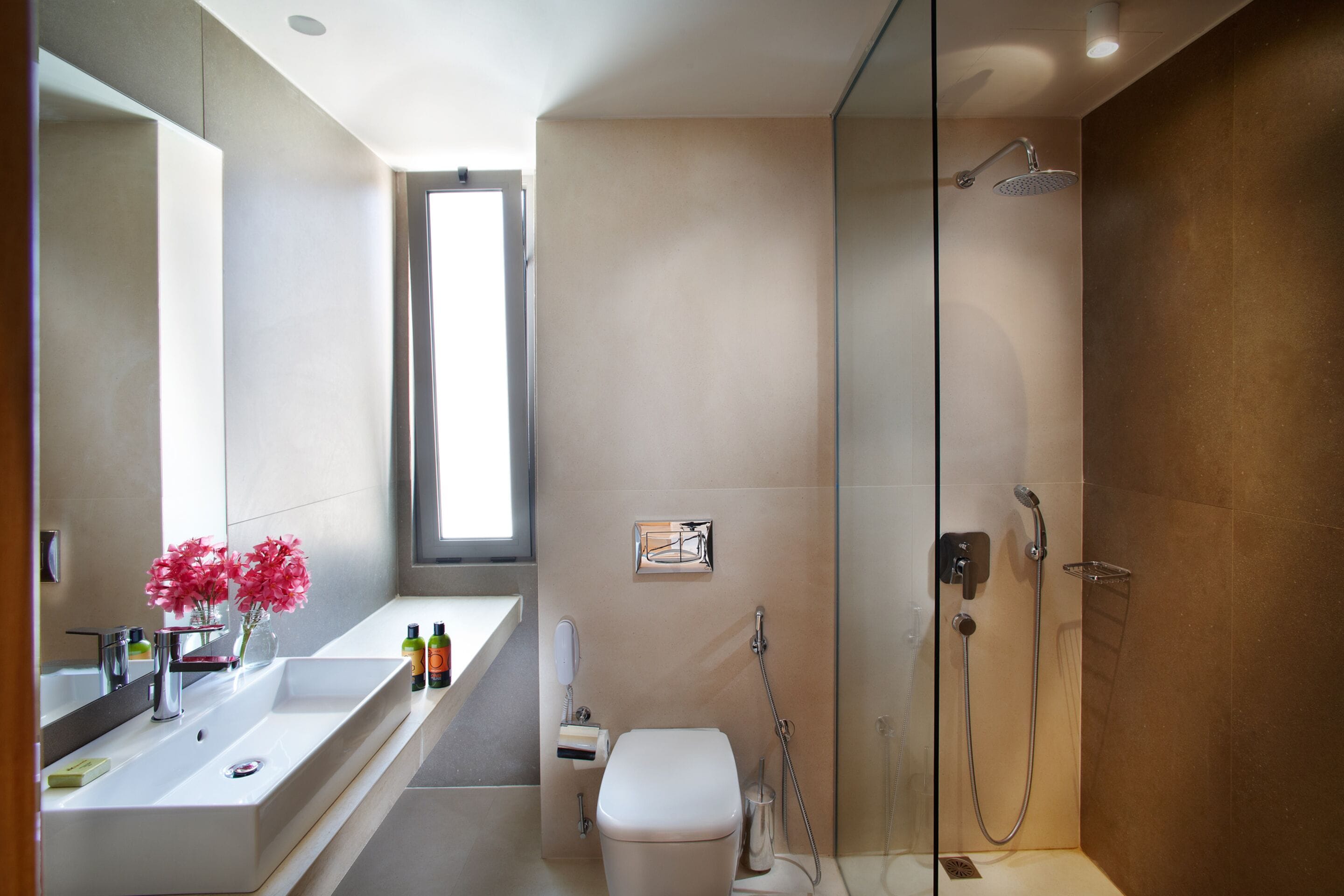 Un baño moderno con un espejo grande, un lavamanos blanco, un inodoro y una ducha.