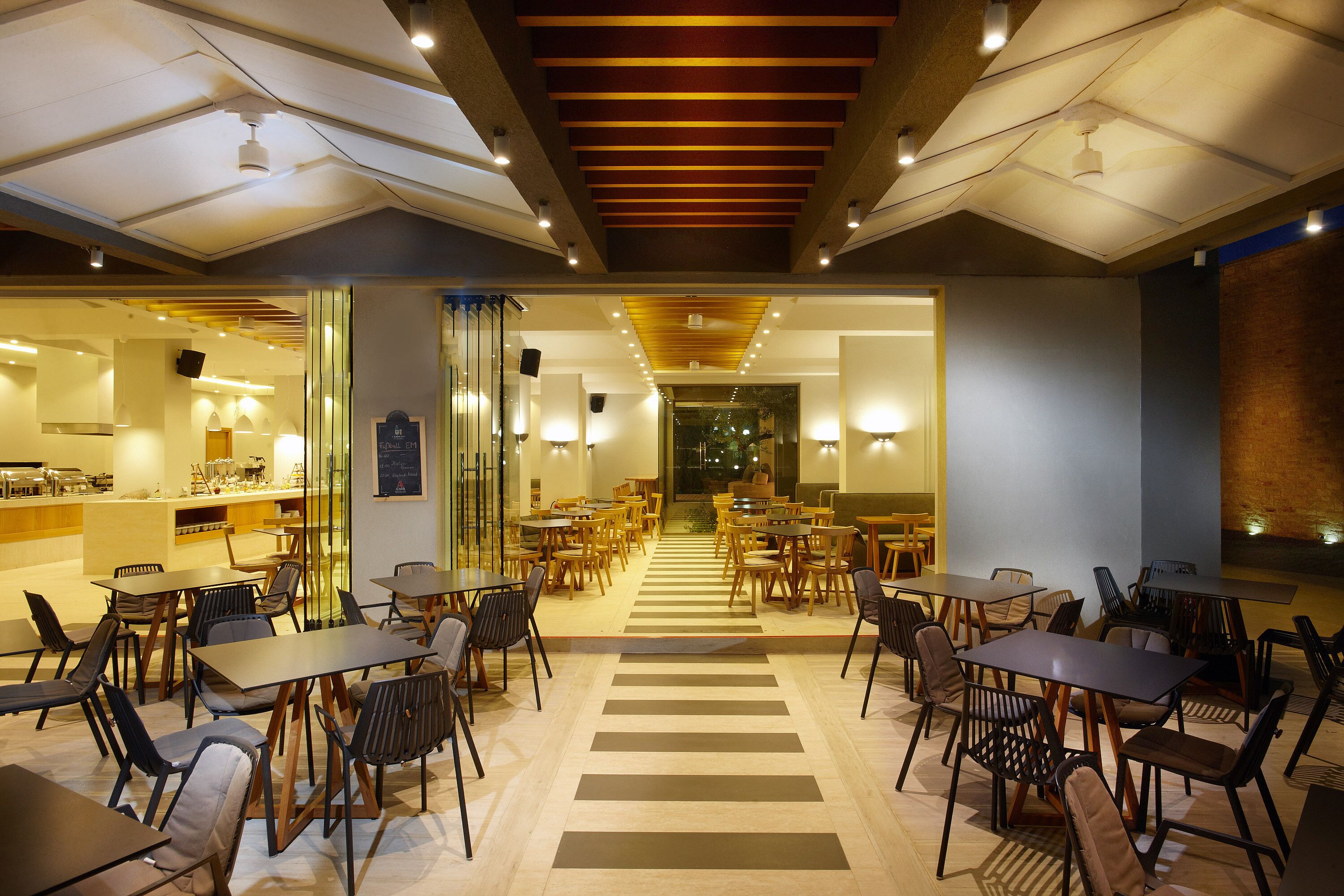 Un restaurant modern amb un passadís central que condueix a una zona de bar, envoltat de taules i cadires.