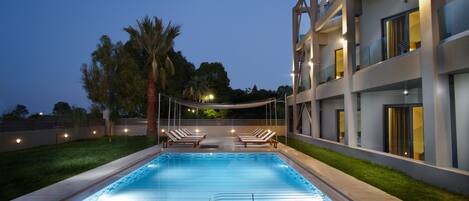 Una piscina con sillas de descanso, una palmera y un edificio moderno con balcones.
