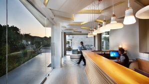 A modern reception area with a wooden reception desk, a large window offering a view of the outdoors, and pendant lighting. - Annas House (Apokoronas)