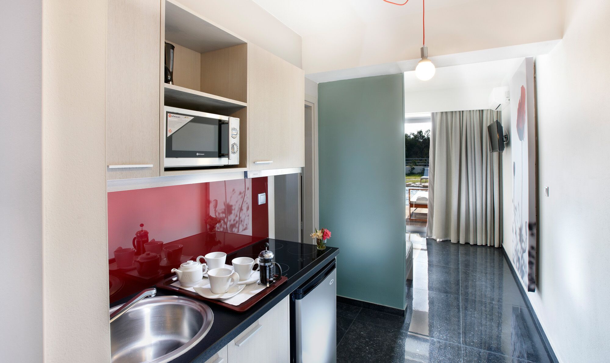Cocina compacta con microondas, cafetera y pileta. Pequeño comedor con mesa y sillas.