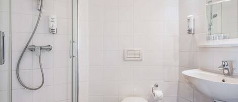 A modern bathroom with a glass shower enclosure, a white toilet, a sink with a mirror, and a towel dispenser.