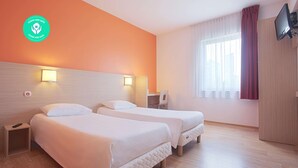 Habitación de hotel con dos camas, televisión, escritorio y ventana con cortinas.