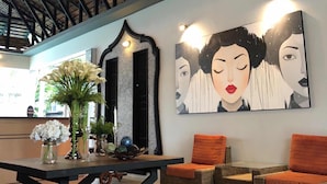 A spacious lobby with a high ceiling, a reception desk, wicker chairs, and a large abstract painting. - Paragon Inn (Bang Phli)