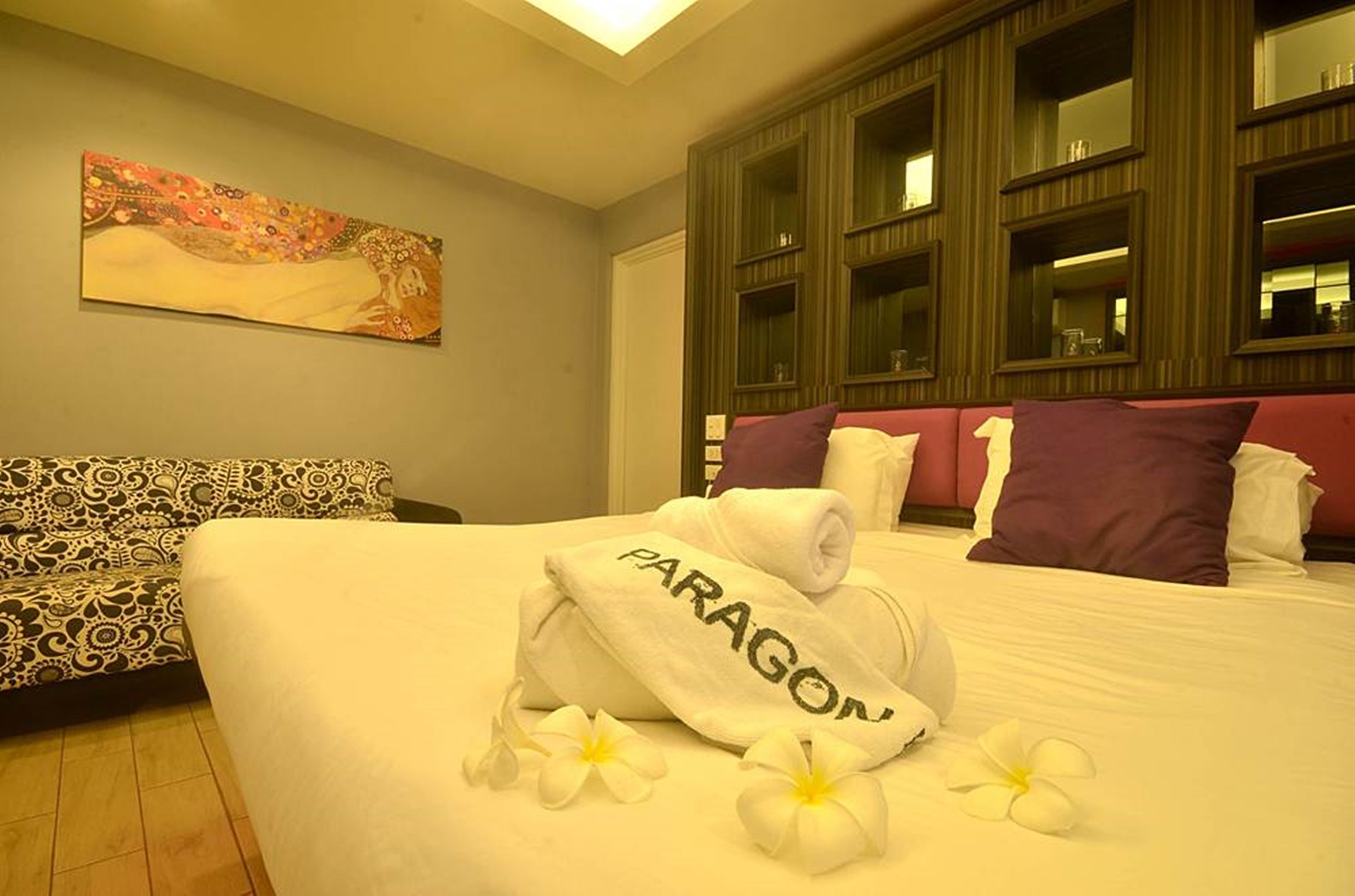 A hotel room with a large bed, a patterned sofa, a painting on the wall, and built-in shelving.