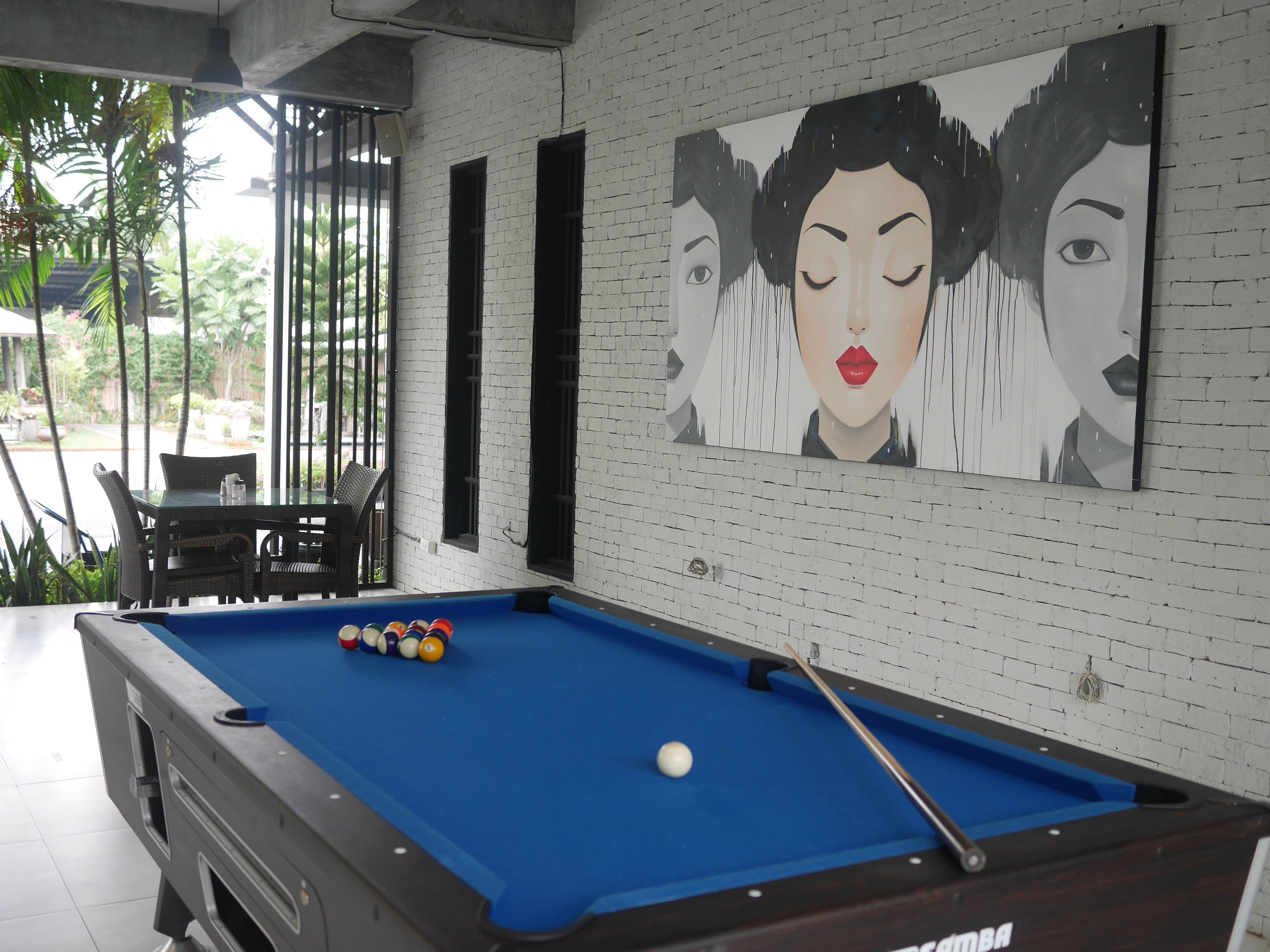 A pool table with balls, a cue stick, and a painting on the wall.