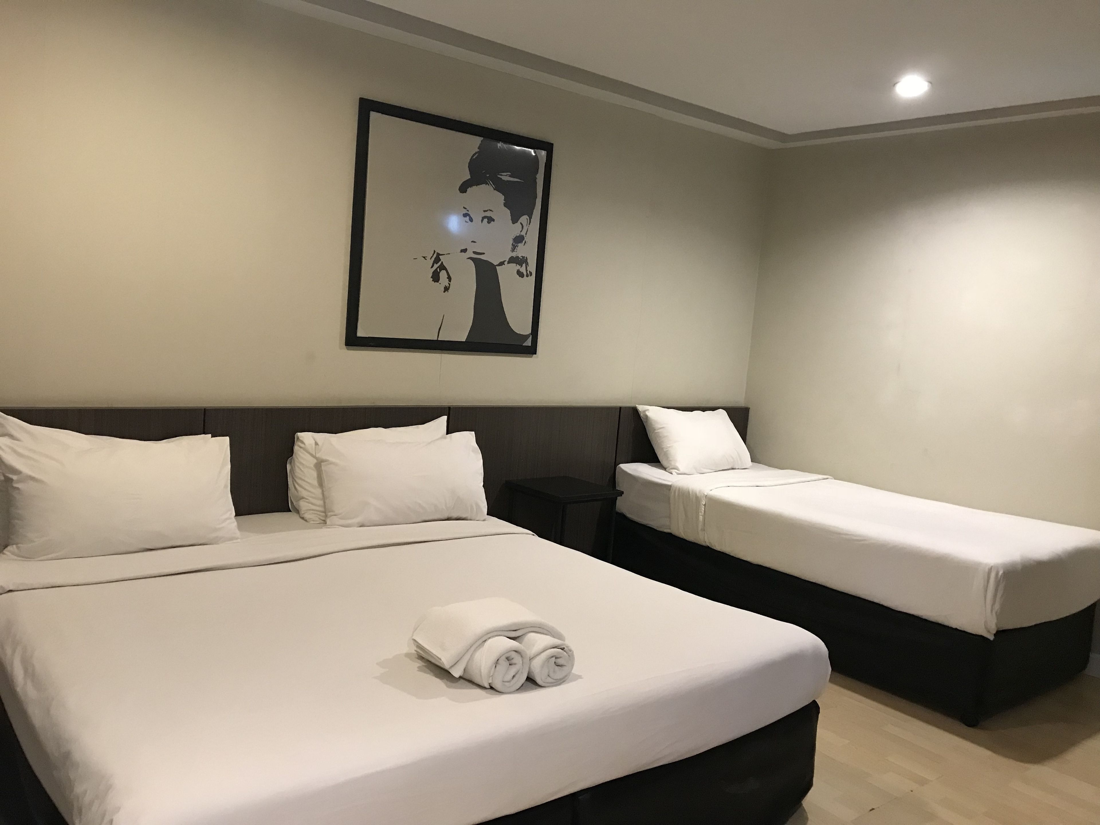 Ein Hotelzimmer mit einem großen Bett, zwei Einzelbetten, weißer Bettwäsche, einem gerahmten Bild an der Wand und einem kleinen Tisch.