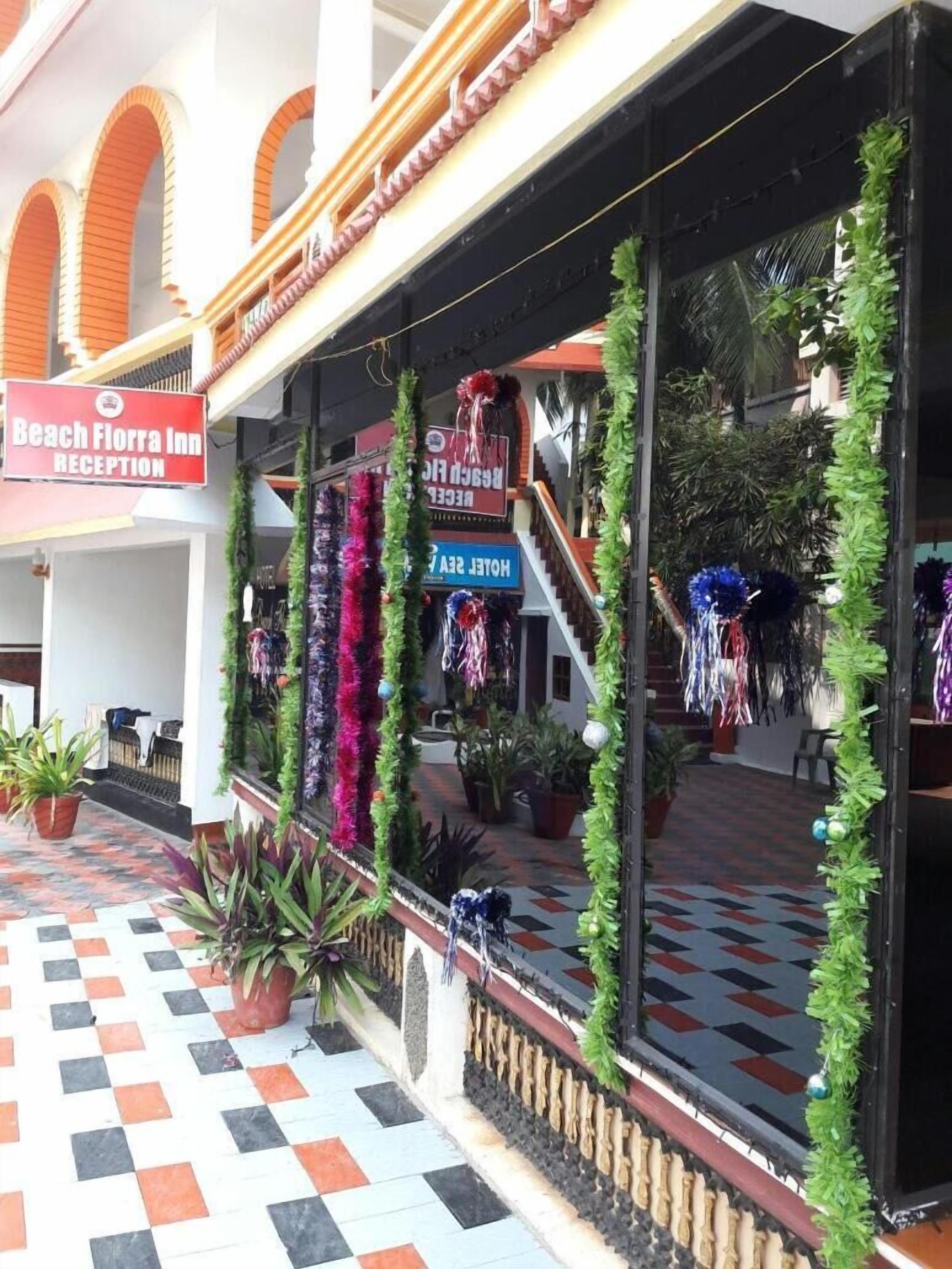 Zona de recepción de hotel con piso a cuadros, plantas en macetas y una escalera que sube a un nivel superior.