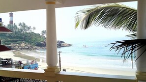A beach view from a balcony with a palm tree, a lighthouse, and a beach bar area. - Beach Florra Inn (Neyyattinkara)