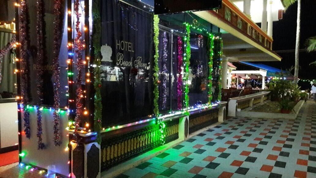 Fachada de hotel con la señalización 'HOTEL Beach Flora', decorada con luces y guirnaldas coloridas.