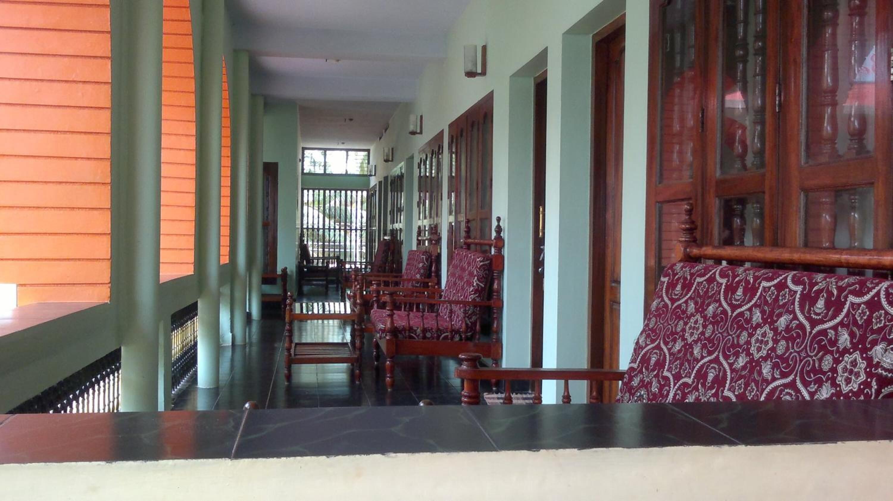 A corridor with wooden chairs and benches, a tiled floor, and a view through a window.