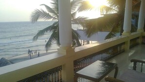 A balcony with a view of the ocean, palm trees, and a railing.