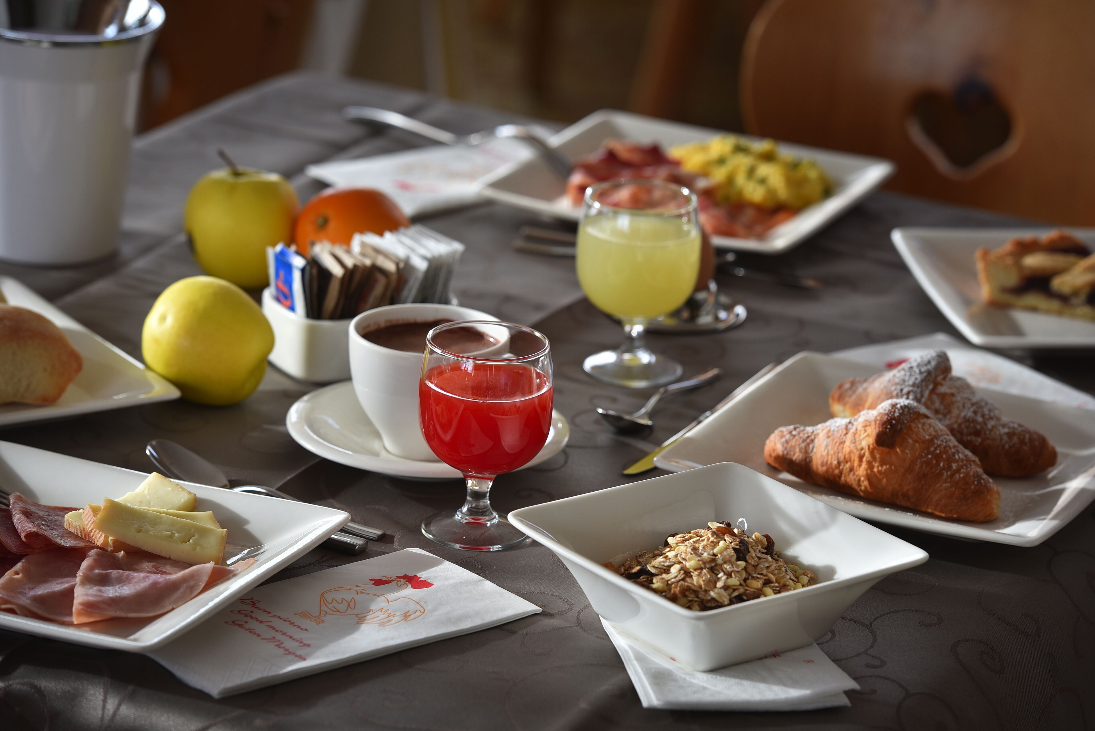 Una colazione con diversi piatti, tra cui croissant, frutta e una bevanda rossa.