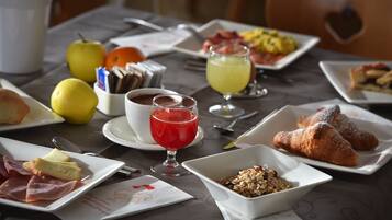 Una colazione con diversi piatti, tra cui croissant, frutta e una bevanda rossa.
