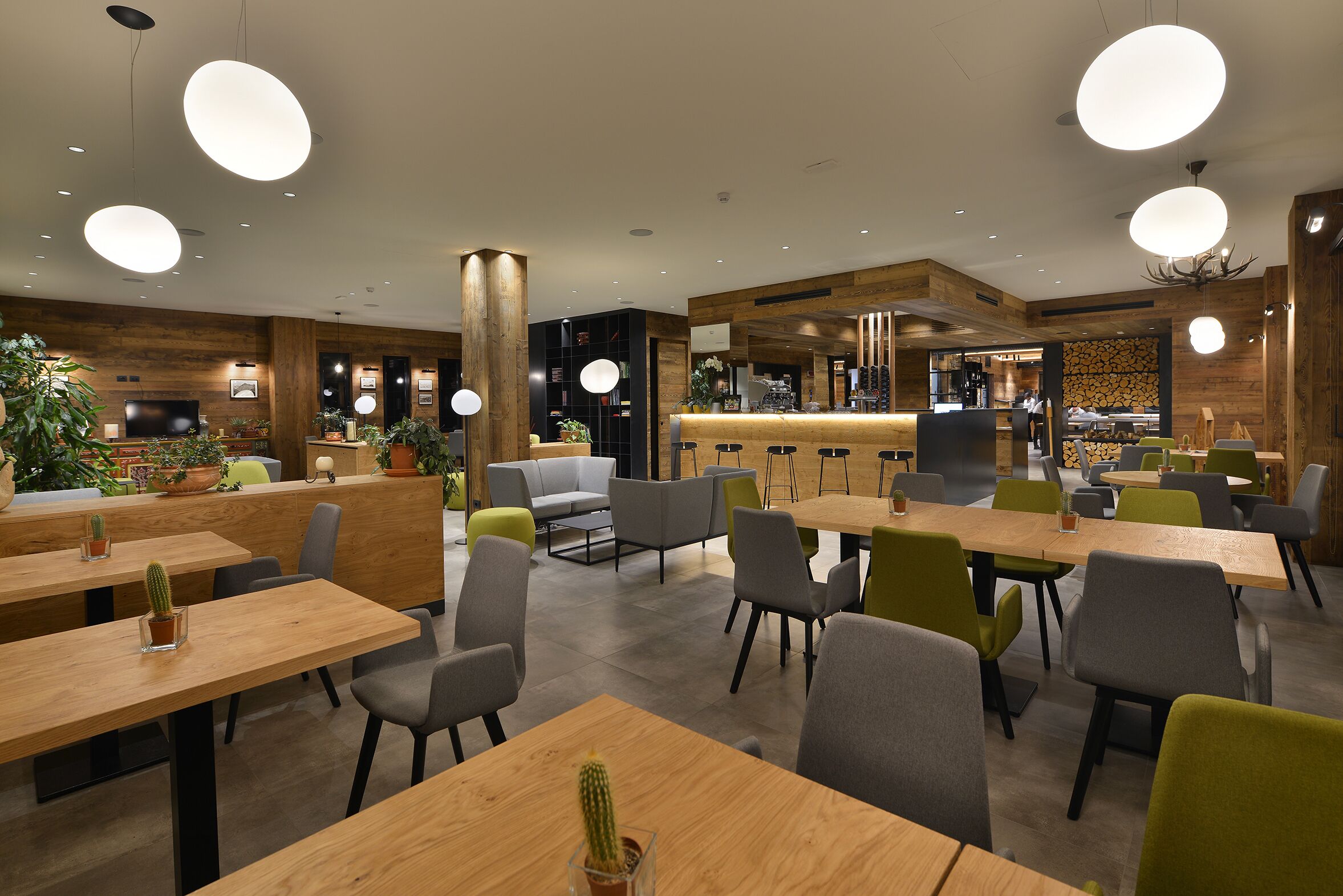Un ristorante moderno con tavoli in legno, sedie grigie e verdi, e lampade a sospensione.