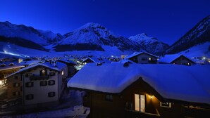 A snow-covered mountain village at night with illuminated buildings and a clear view of the surrounding peaks. - Hotel Bernina (Livigno)