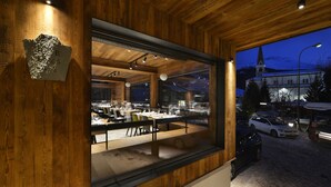 A restaurant with a wooden interior and a view of a snowy mountain and church at night. - Hotel Bernina (Livigno)