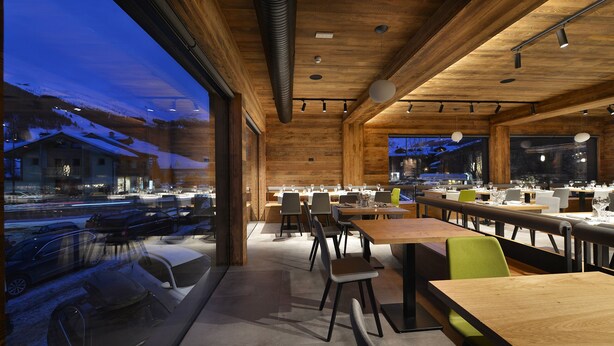 A modern restaurant with wooden interiors, large windows, and a view of a snowy landscape. - Hotel Bernina (Livigno)