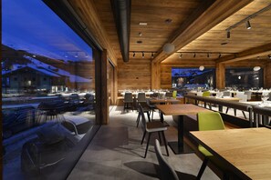 A modern restaurant with wooden interiors, large windows, and a view of a snowy landscape. - Hotel Bernina (Livigno)